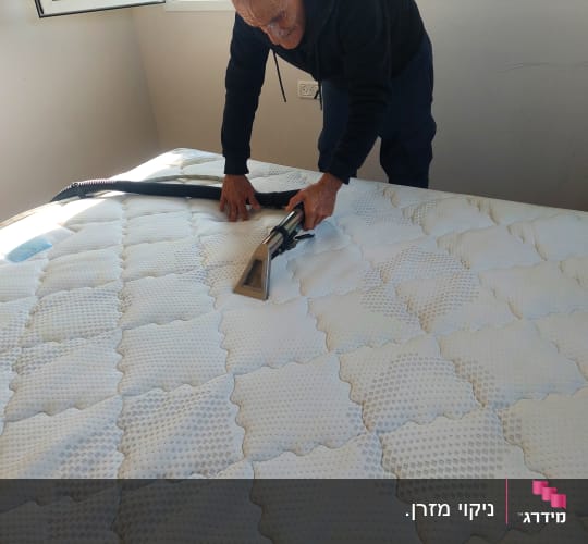 אדם מנקה מזרן עם שואב אבק ידני